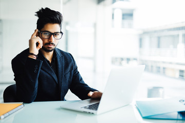 Fototapeta premium Confused indian businessman working on laptop in office. Young indian man thinking over project at his desk with laptop.