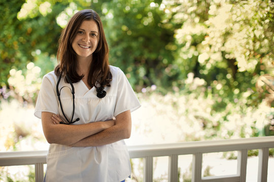 Portrait of young female nurse standing on the verandah of someone's home.