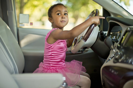 Young girl dressed as a ballerina pretending to drive a car.