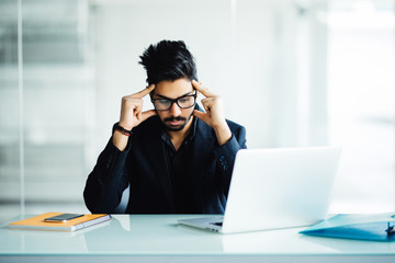 Closeup portrait of a busy guy in deep thought while looking at his laptop in office
