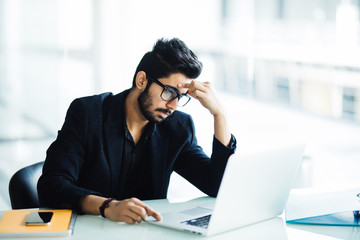 Photo of an Indian male frustrated with work sitting in front of a laptop in modern office