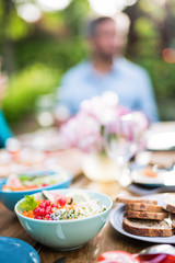 Close-up on a colorful salad in a bowl, Friends gather to share a meal around a table in the garden. Focus on the foreground