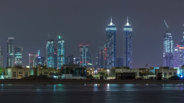 Modern Dubai city skyline timelapse at night with illuminated skyscrapers over water surface