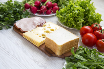 Set of ingredients for making school lunch: sandwich, vegetables, cheese and bacon on white wooden background. Healthy eating concept, side view