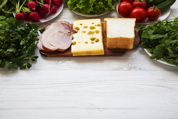 Set of ingredients for making school lunch: sandwich, vegetables, cheese and bacon on white wooden background. Healthy eating concept, side view. Copy space.