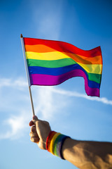 Colorful backlit rainbow gay pride flag being waved in the breeze against a sunset sky.