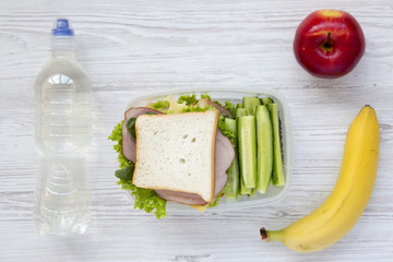 Healthy school lunch box with fresh organic vegetables sandwich, fruits and bottle of water on white wooden background, flat lay. From above.
