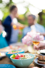 Close-up on a colorful salad in a bowl, Friends gather to share a meal around a table in the garden. Focus on the foreground