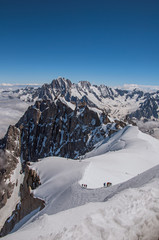 Snowy peaks and mountaineers in a sunny day, viewed from the Aiguille du Midi, near Chamonix. A famous ski resort located in Haute-Savoie Province, at the foot of Mont Blanc in the French Alps.