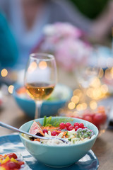 Close-up on a colorful salad in a bowl, Friends gather to share a meal around a table in the garden. Focus on the foreground