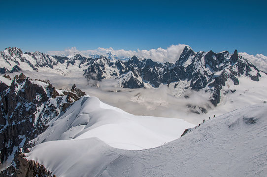 Snowy peaks and mountaineers in a sunny day, viewed from the Aiguille du Midi, near Chamonix. A famous ski resort located in Haute-Savoie Province in the French Alps. Retouched photo.