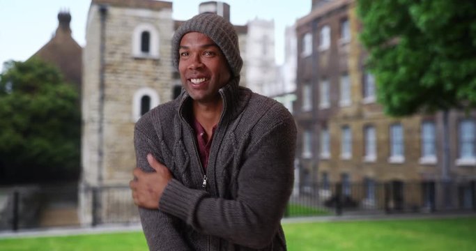 Young African man visiting England wearing winter attire standing outside on a brisk morning, Shivering young African-American tourist on a cold day in England, 4k