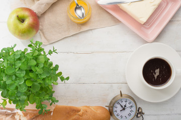 Morning cup of coffee, alarm clock, apples, butter and baguette, in a light kitchen. Background area, the concept of a bright morning and breakfast. Top view, with empty space for inscription