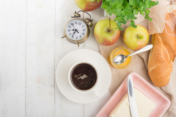 Morning cup of coffee, alarm clock, apples, butter and baguette, in a light kitchen. Background area, the concept of a bright morning and breakfast. Top view, with empty space for inscription
