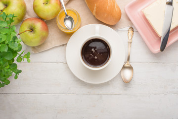 Morning cup of coffee, alarm clock, apples, butter and baguette, in a light kitchen. Background area, the concept of a bright morning and breakfast. Top view, with empty space for inscription