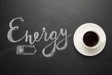 White cup of coffee on a dark texture with an inscription of energy and a battery! The concept of...