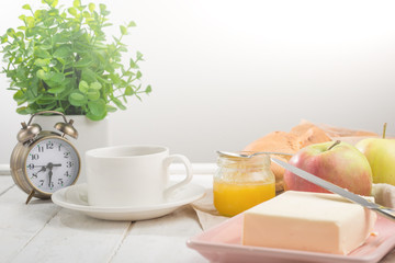Morning cup of coffee, alarm clock, apples, butter and baguette, in a light kitchen. Background area, the concept of a bright morning and breakfast