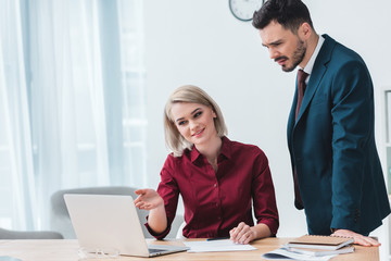 smiling young business people working together and looking at laptop in office