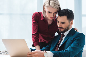 Fototapeta premium young coworkers using laptop and flirting in office