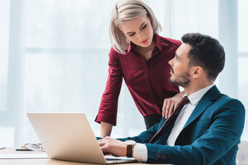 attractive young woman and handsome businessman flirting and looking at each other in office