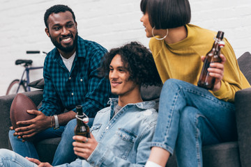 young multicultural friends with bottles of beer and ball for american football