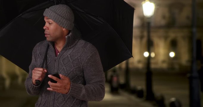 African-American male in Paris, France standing outside with an umbrella on a chilly night, Black young man in a sweater and beanie holding an umbrella outside, 4k