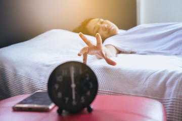 Woman hates getting stressed waking up early in bedroom,Female stretching her hand to ringing alarm...