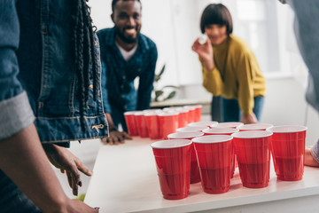 cropped shot of multicultural group of friends playing beer pong at table - Powered by Adobe