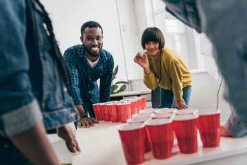 cropped image of multicultural group of friends playing beer pong at table