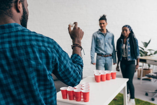 cropped image of young african american man preparing to throw ball in beer pong game
