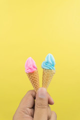 hand holding the mini strawberry and blueberry soft ice cream in wafer cones on yellow background