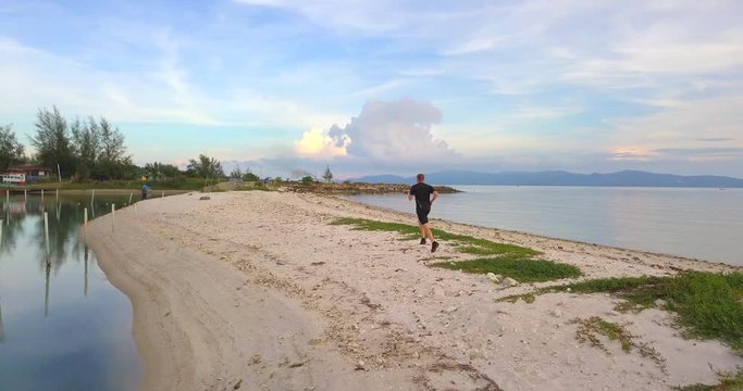 Running athlete man jogging at sunset beach. Fitness runner training outside by the sea coast line in beautiful sunset or sunrise in full body length in summer time,tracking follow shot