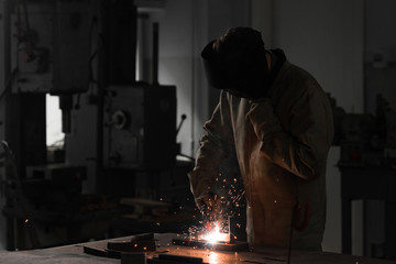 front view of worker in protection mask welding metal at factory