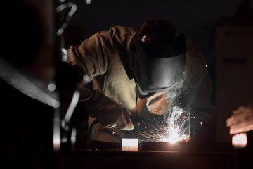front view of welder in protection mask working with metal at factory
