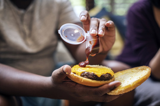 Man adding some ketchup to a burger - Powered by Adobe