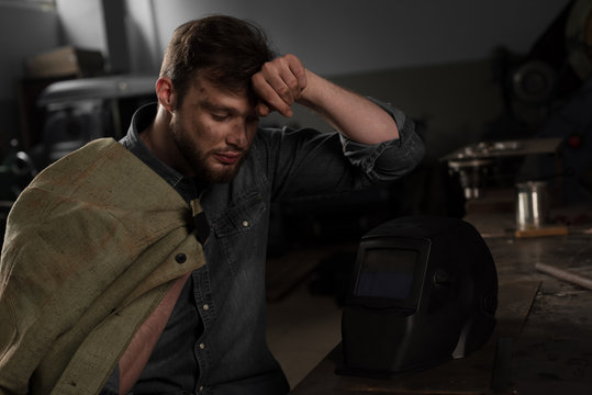 Tired Workman With Uniform On Shoulder Sitting At Table With Protective Mask