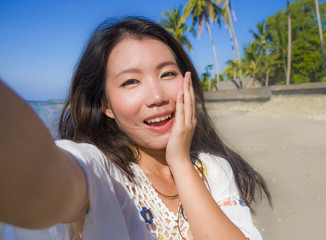 self portrait of gorgeous beautiful and happy Asian Korean or Chinese woman 20s taking selfie photo with mobile phone camera in exotic tropical beach