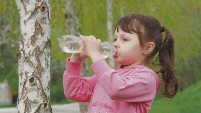 The child drinks water. A girl is drinking water in nature.