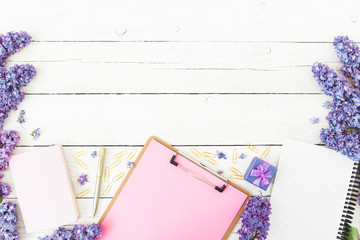 Minimalistic composition with clipboard, notebook, lilac flowers, gift box and accessories on wooden background. Flat lay, top view. Beauty blog concept. Frame