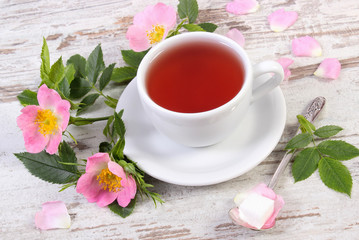 Cup of tea and wild rose flower on old rustic board