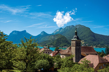 View of houses and belfry with blue sky mountains landscape on background, in the village of Talloires. A lovely village next to the Lake of Annecy. Department of Haute-Savoie, southeastern France.