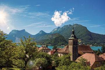 Fototapeta na wymiar View of houses and belfry with blue sky mountains landscape, in the village of Talloires. A lovely village next to the Lake of Annecy. Department of Haute-Savoie, southeastern France. Retouched photo