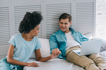 African american girl holding hand of her boyfriend in bed with laptop