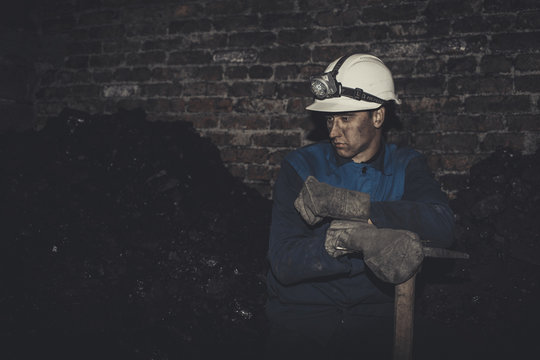 a miner with a pick sitting on the corner all tired and dirty from the coal dust after a hard work in the mine