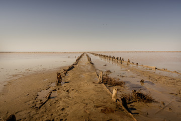 Pink salty lake with an old wooden pier. An ancient method of extracting salt from the sea.