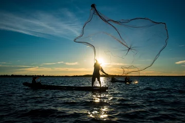 Unbekannter Silhouettenfischer beim Bootsfischen durch Werfen von Fischernetzen © goldquest