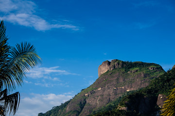 Fototapeta na wymiar View of the Gavea Stone, seen from the street with houses on the hill during late afternoon. Barra da Tijuca, Rio de Janeiro
