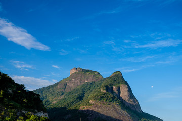 Fototapeta premium View of the Gavea Stone, seen from the street with houses on the hill during late afternoon. Barra da Tijuca, Rio de Janeiro