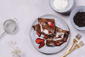 Homemade chocolate crepes with strawberry and cream on grey concrete background. Delicious breakfast. Selective focus