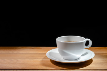 coffee cup with saucer on wooden table on black background